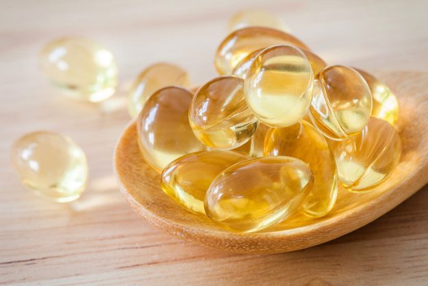 fish oil supplement capsule on wooden spoon and wooden background