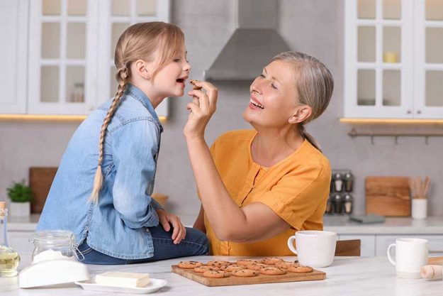 happy grandmother feeding her granddaughter cookie kitchen