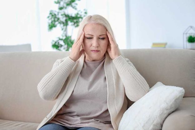 mature woman suffering from headache while sitting on sofa at home mature woman suffering from headache while sitting on sofa at home