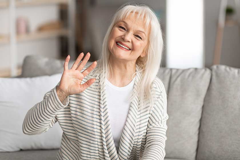 mature woman waving at camera and smiling sitting on sofa