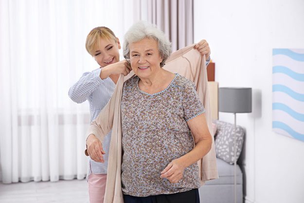 caregiver helping senior woman to put on cardigan at home caregiver helping senior woman to put on cardigan at home