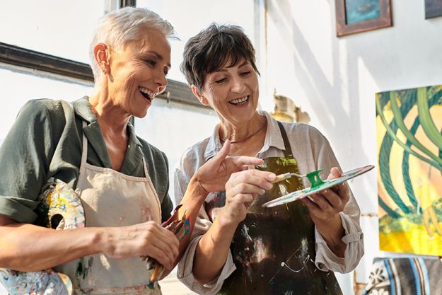cheerful female artist helping mature woman mixing paints palette master