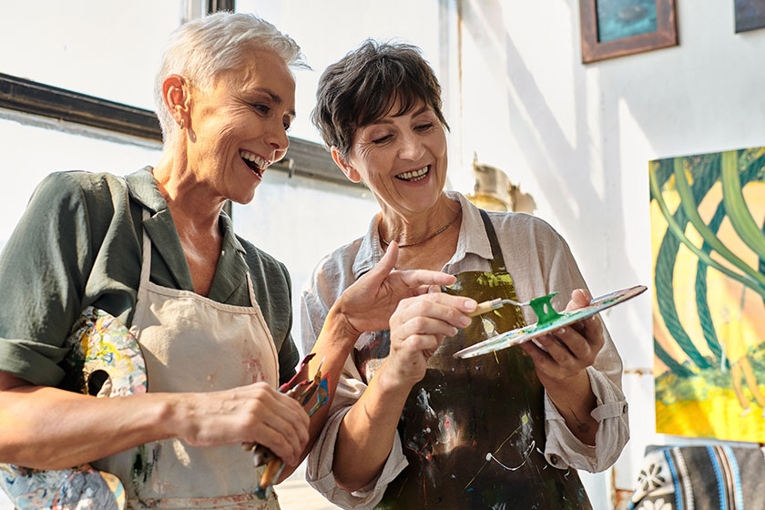 cheerful female artist helping mature woman mixing paints palette master