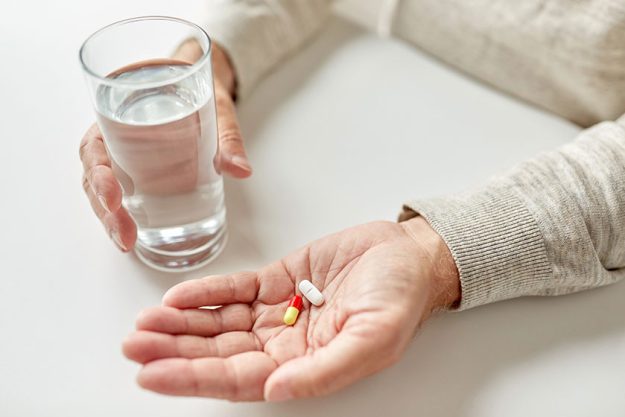 close up of old man hands with pills and water