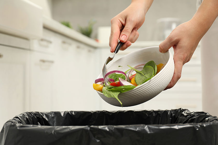 woman throwing vegetable salad bin indoors closeup