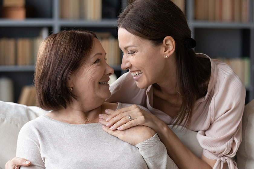 young woman embracing from back sitting on sofa older mother