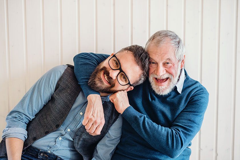 A portrait of adult hipster son and senior father sitting on floor indoors at home