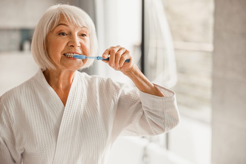 elderly woman in bathrobe brushing teeth in the morning