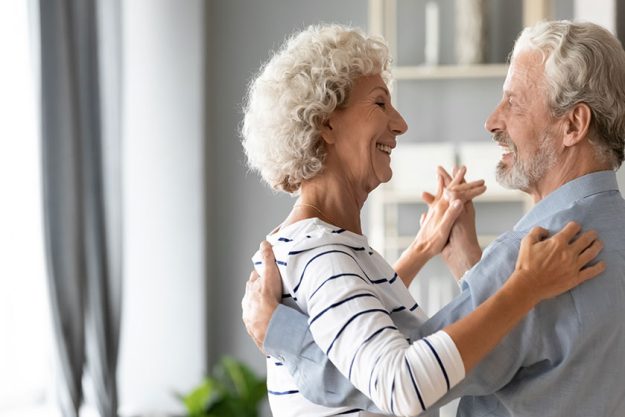 Happy romantic older retired family couple dancing at home