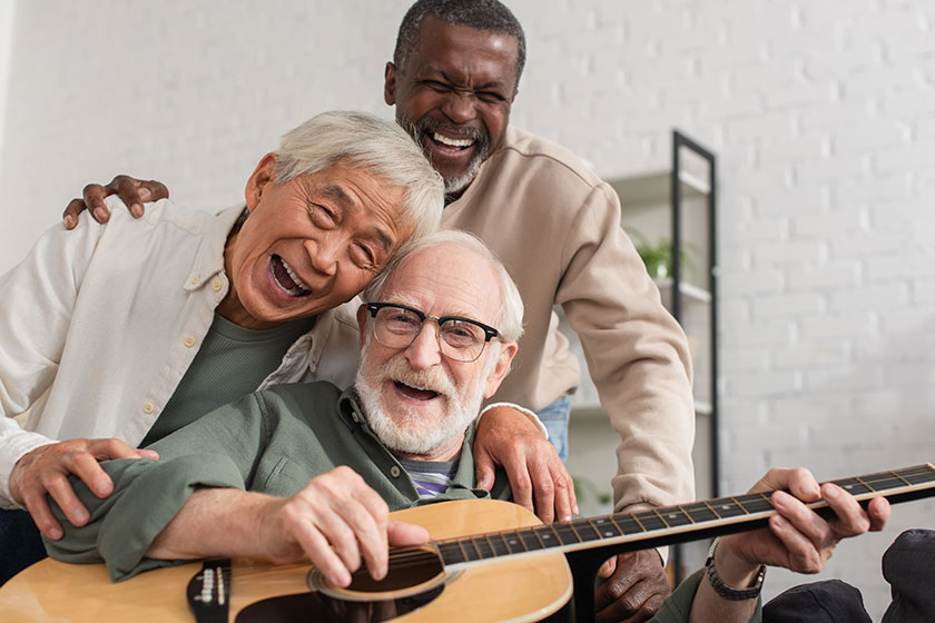 Happy senior interracial friends playing acoustic guitar looking camera home Happy senior interracial friends playing acoustic guitar looking camera home