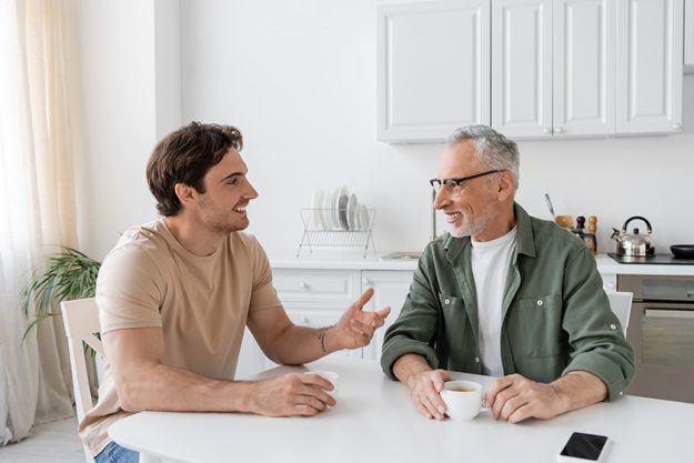 happy young man gesturing while talking father breakfast home