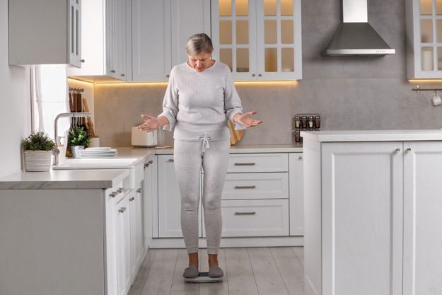 Menopause weight gain concerned woman standing floor scales kitchen Menopause weight gain concerned woman standing floor scales kitchen