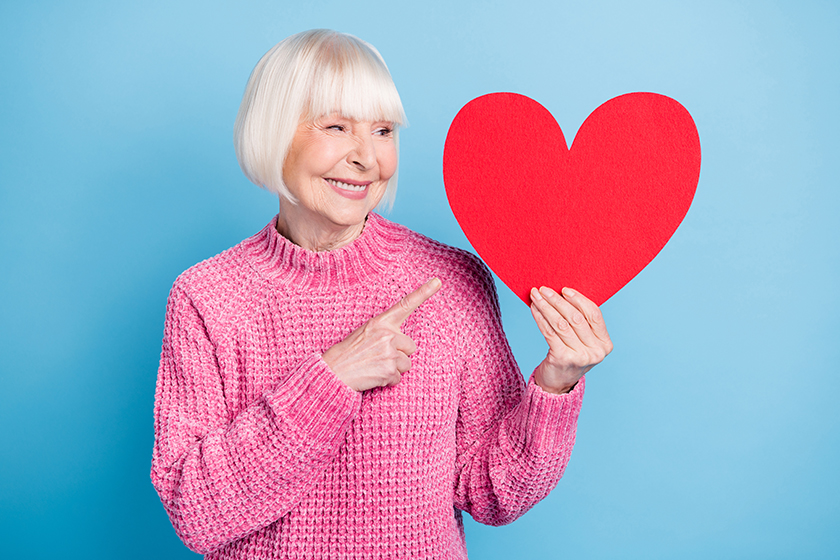 photo portrait of old woman looking pointing finger at big red heart card holding in