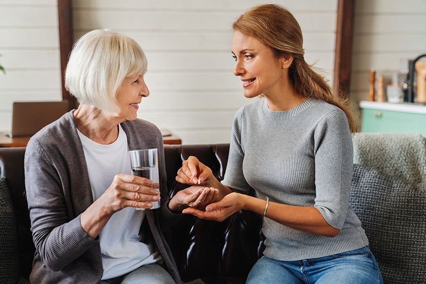 Senior woman taking pills her daughter while holding glass water