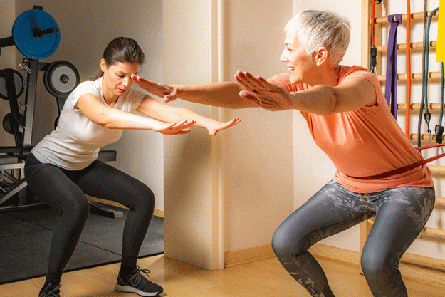 active senior woman doing squats female instructor helping her