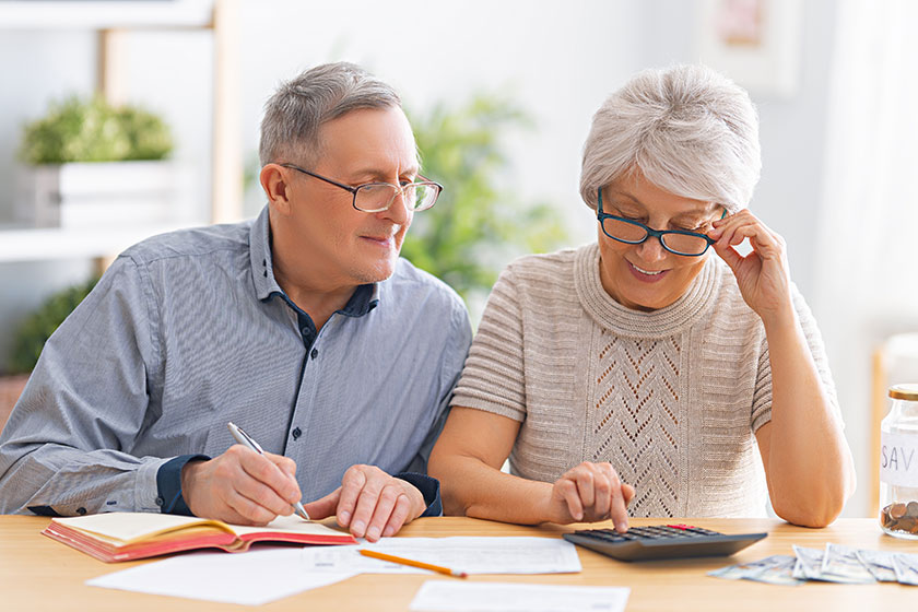 elderly married couple sitting desk paper receipt hands calculating expenses