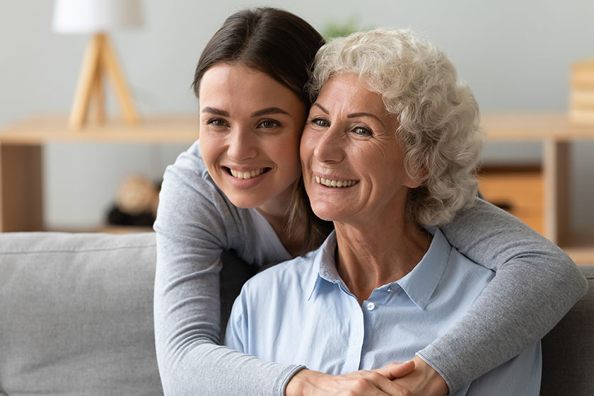 happy adult granddaughter hugs from behind old grandmother