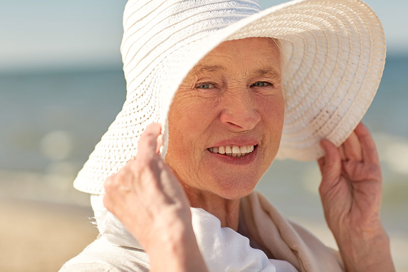 happy senior woman in sun hat on summer beach