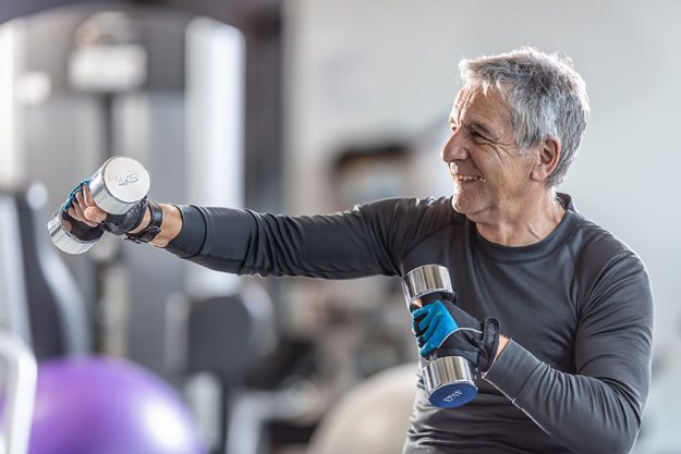 older man working out dumbbells gym smiling