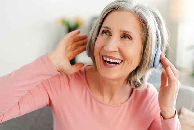 overjoyed senior woman listening music wireless headphones having fun sitting