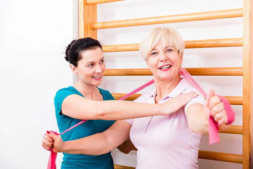 physio assisting elderly woman during exercise with power band