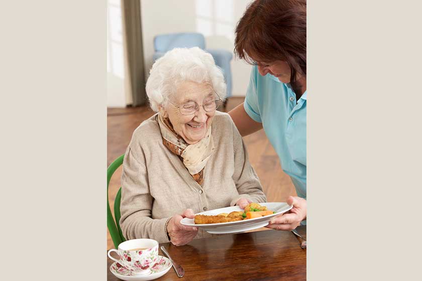 senior woman being served meal by carer