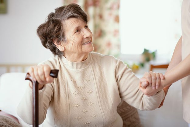 smiling senior woman walking stick helpful caregiver holding her hand