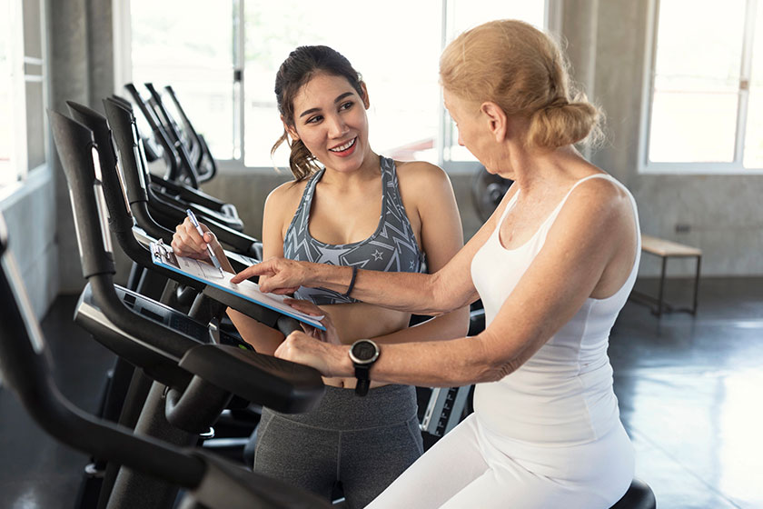 trainer with senior woman exercising spinning bike in fitness trainer with senior woman exercising spinning bike in fitness