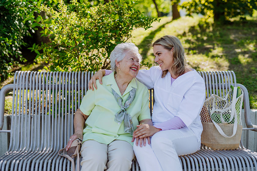 A caregiver with senior woman sitting on bench in park