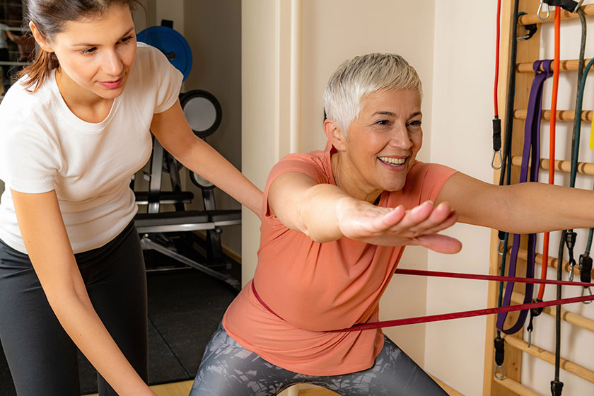 Active senior woman doing squats female instructor helping her