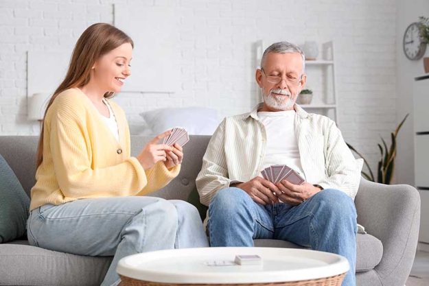 female caregiver senior man playing cards nursing home