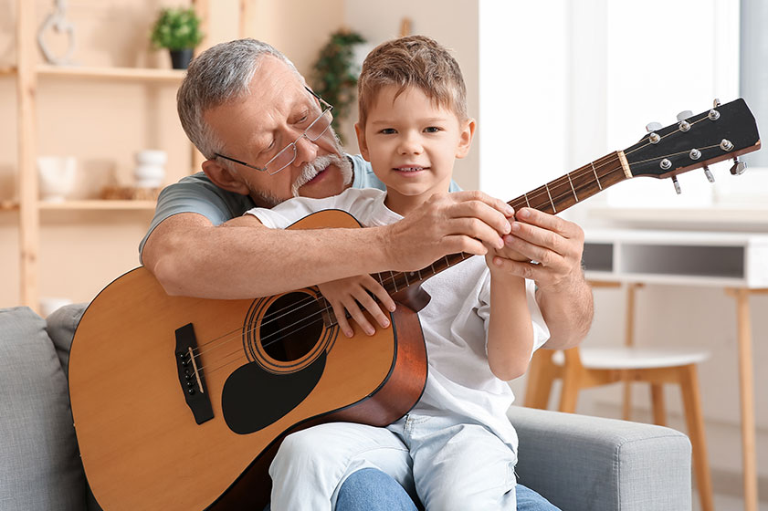Grandfather teaching his cute little grandson playing guitar home