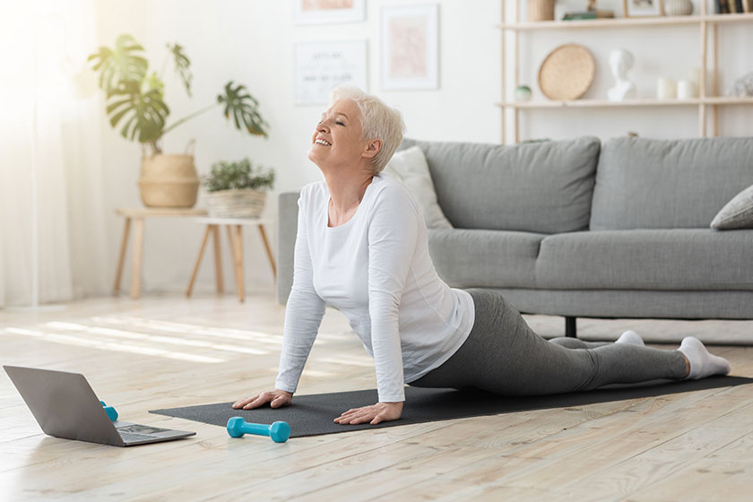 Online yoga senior woman standing in cobra pose in front of laptop