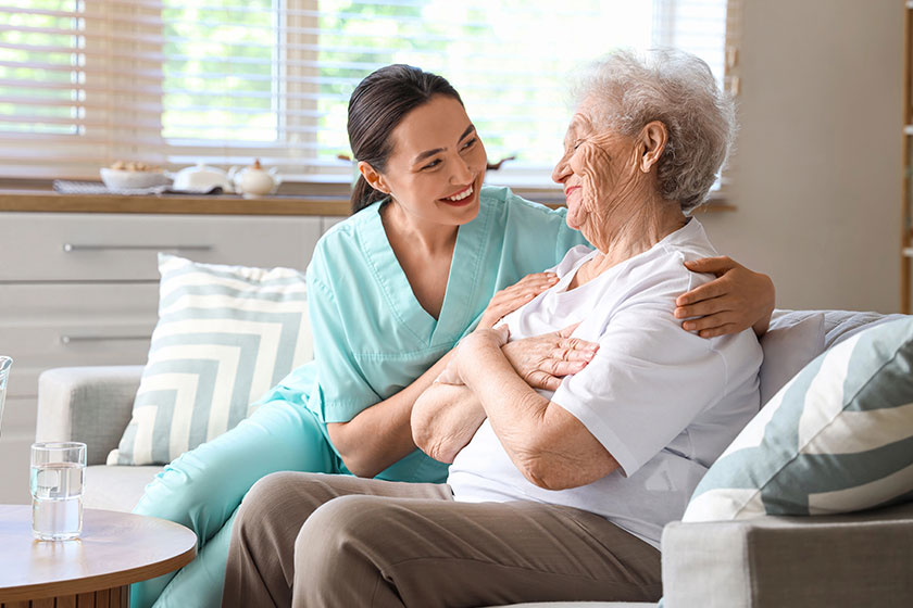 Physical therapist hugging senior woman sofa home Physical therapist hugging senior woman sofa home