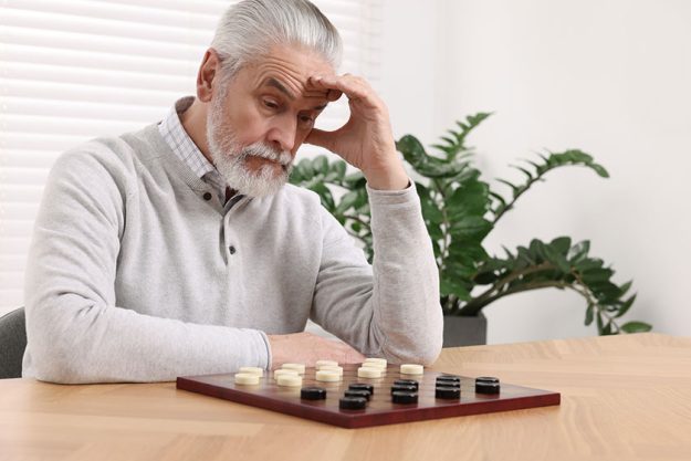 playing checkers concentrated senior man thinking next move table room