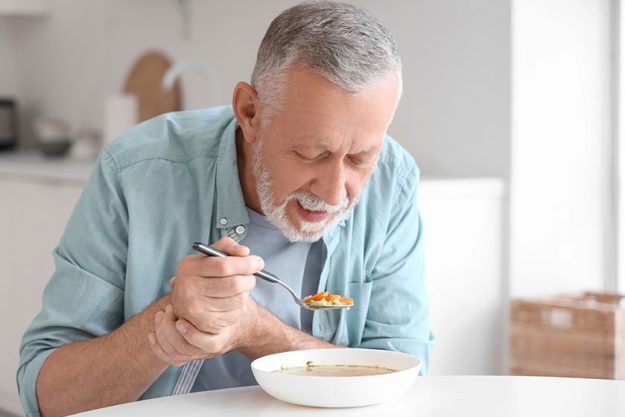 Senior man suffering parkinson syndrome eating table kitchen Senior man suffering parkinson syndrome eating table kitchen