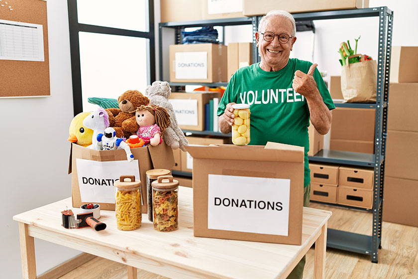 senior man volunteer holding donations box putting food box smiling Senior man volunteer holding donations box