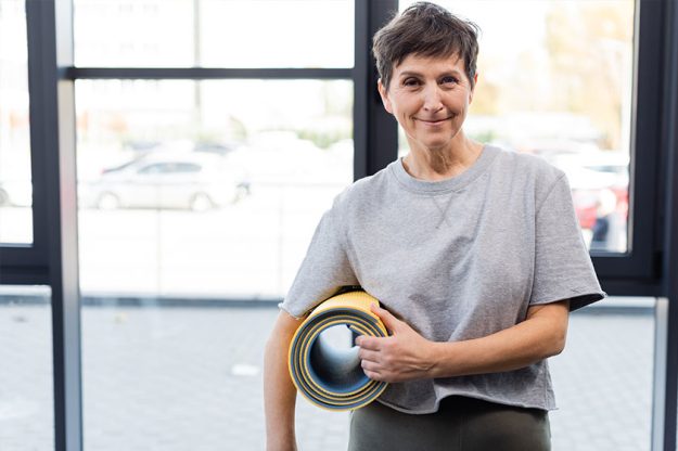 Smiling senior sportswoman holding fitness mat