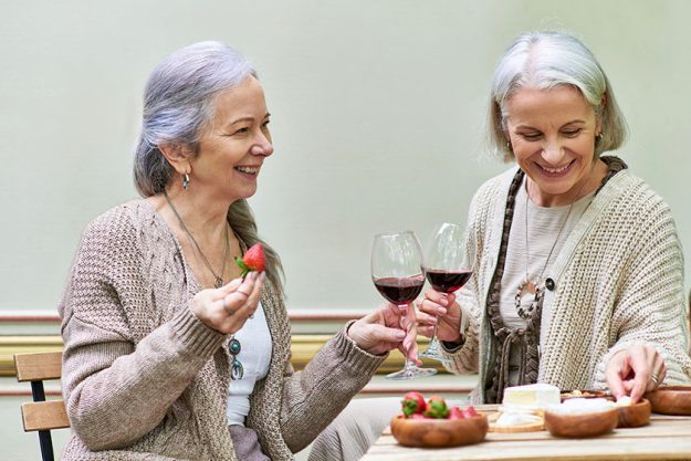 Two middle aged women enjoy wine strawberries together while camping