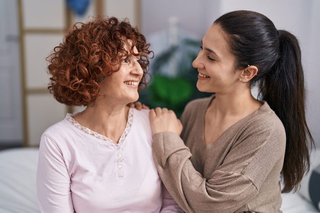 Two women mother daughter hugging each other sitting bed Two women mother daughter hugging each other sitting bed