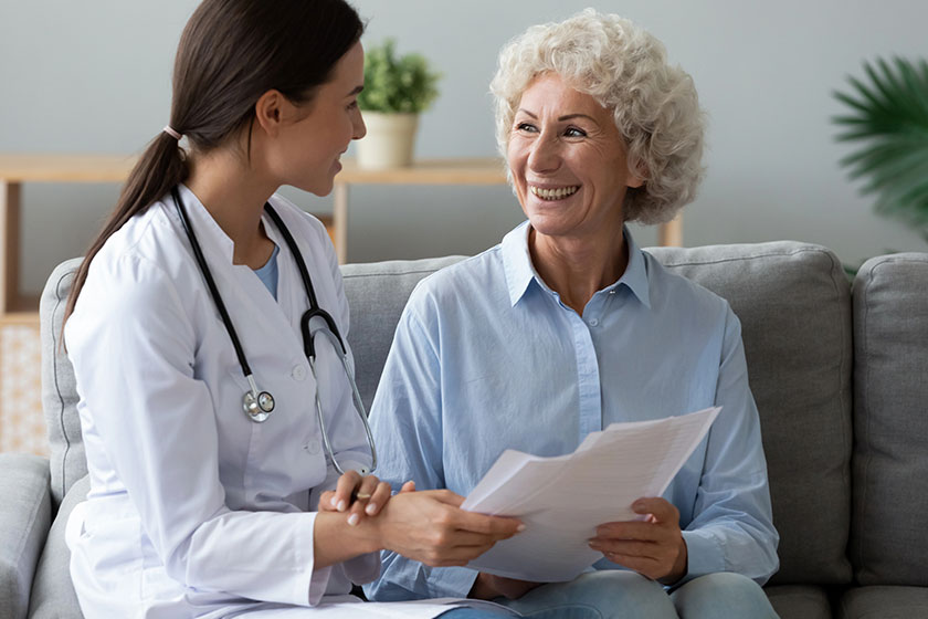 Young woman doctor consult happy old grandmother patient hold papers