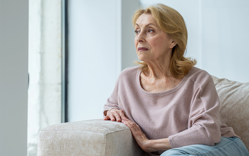 A thoughtful elderly woman is sitting on the sofa in the living room looking out A thoughtful elderly woman is sitting on the sofa in the living room looking out