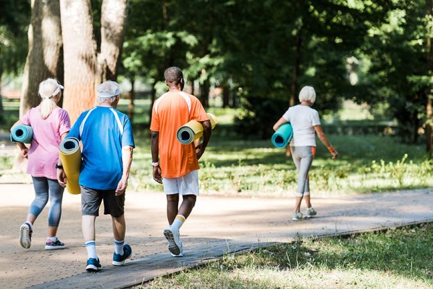 Back view happy senior multicultural pensioners holding fitness mats walking Back view happy senior multicultural pensioners holding fitness mats walking