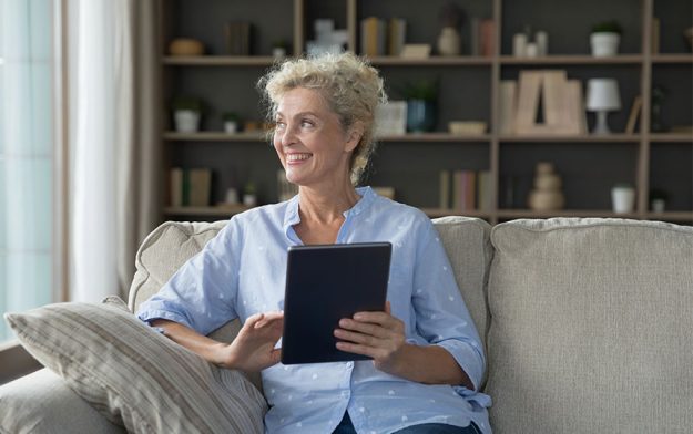Dreamy mature attractive woman holding digital tablet device look away