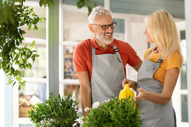 Happy senior man woman aprons watering flowers chatting smiling mature Happy senior man woman aprons watering flowers chatting smiling mature