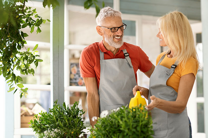 Happy senior man woman aprons watering flowers chatting smiling mature Happy senior man woman aprons watering flowers chatting smiling mature