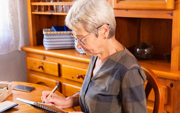 Senior mature caucasian woman making notes while sitting table
