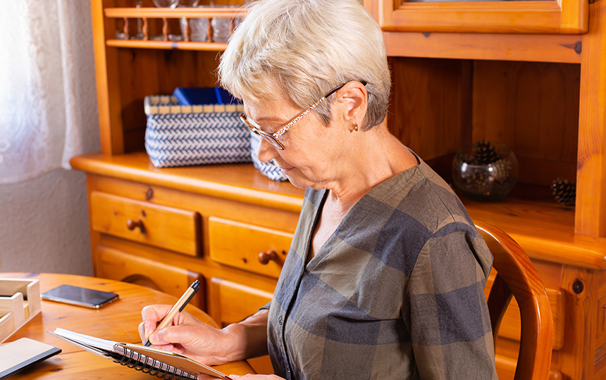 Senior mature caucasian woman making notes while sitting table