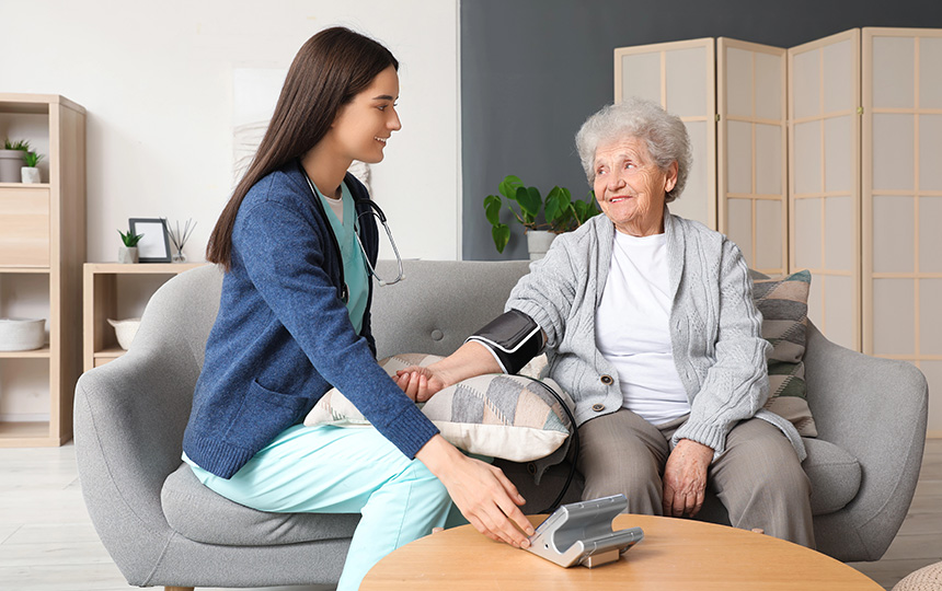 Young caregiver measuring blood pressure senior woman home