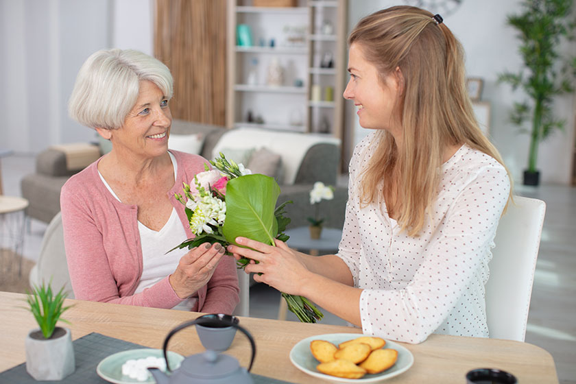 Beautiful adult woman giving flowers her mature mother